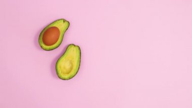 Pastel pembe arka planda, ortasında yumurta olan dilimlenmiş avokado. Hareketi durdur