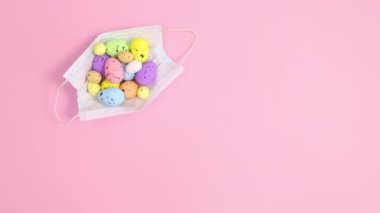 Paskalya yumurtaları ve pastel pembe arka planda hareket eden yüz maskesi. Dur hareketi düz yatıyordu