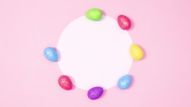 Paskalya yumurtaları pastel pembe arka planda kağıt kart etrafında belirir. Hareketi durdur