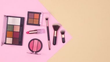 Makyaj fırçaları paletler ve rujlar pastel pembe ve bej arka planda görünür. Hareketi durdur