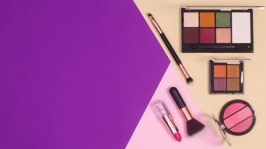 Makyaj ürünlerinin minimum düzlem düzeni mor pastel pembe ve bej arka planda görünür. Hareketi durdur