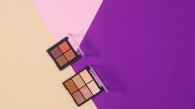 Göz farı paletleri ve fırçalar mor, pastel pembe ve bej arkaplanda görünür. Hareketi durdur