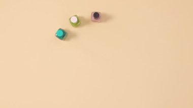 Manikür tırnak cilası şişeleri farklı renklerde parlatır, bej arka planda fotokopi alanı oluşturur. Dur hareketi düz yatıyordu