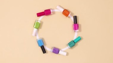 Tırnak cilasının yaratıcı hareketi şişeleri bej arka planda daire içine alır. Dur hareketi düz yatıyordu