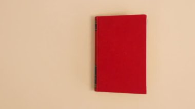 Kırmızı ciltli klasik kitap bej arka planda kopya alanı ile görünür ve açılır. Dur hareketi düz yatıyordu