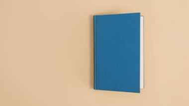 Mavi ciltli klasik kitap bej arka planda kopya alanı ile görünür ve açılır. Dur hareketi düz yatıyordu