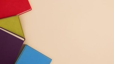 Kırmızı, yeşil, mavi ve mor renkli ciltli kitaplar bej arka planda görünür. Dur hareketi düz yatıyordu