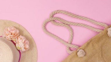 Pastel pembe arka planda çiçekli ve plaj aksesuarlı yaz hasır şapkası görünür. Dur hareketi düz yatıyordu