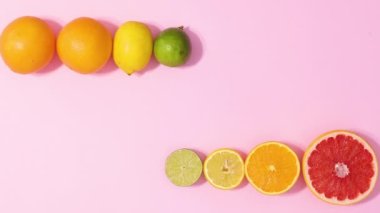 Whole and half citrus fruits ordered in line with green leaves appear on pastel pink background. Stop motion