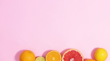 Summer sliced fresh citrus fruits arrangement with leaves appear on bottom on pastel pink background. Stop motion flat lay