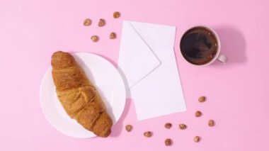 Taze kruvasan ve bir fincan kahve pastel pembe arka planda kağıt kart notlarının etrafında dolaşıyor. Hareketi durdur