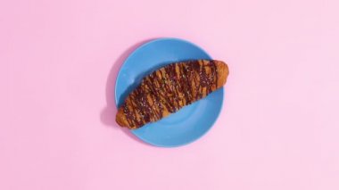 Pastel pembe arka planda mavi tabakta taze çikolatalı kruvasan görünür. Hareketi durdur 