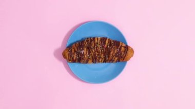 Pastel pembe arka planda mavi tabakta taze çikolatalı kruvasan hareketi. Hareketi durdur 
