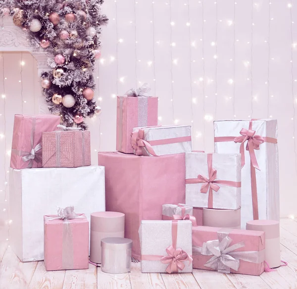 Pastel arka planda Noel süsleri ve ışıkları olan pembe ve beyaz hediye kutuları. Xmas alışverişi, hediye konsepti