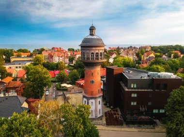 Şafak vakti şehir merkezinde su kulesi alçak evlerin kahverengi çatılarına ve yazın denize karşı.