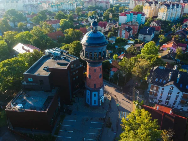 Şafak vakti, şehrin arka planında, alçak evlerin kahverengi çatılarına karşı su kulesi. Zelenogradsk. Rusya