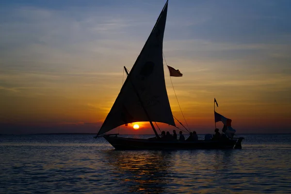 Batan güneşe ve bulutlu gökyüzüne karşı insanlarla birlikte yüzen dhow teknesi. Yüksek kalite fotoğraf. zanzibar