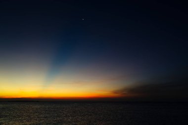 Bulutlu gökyüzünde ay batarken denizde gün batımı. Zanzibar