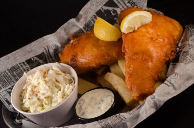 Balık filets derin kızarmış ve altın kahverengi, patates kızartması bir sepet içinde tartar sosu ve bir tarafında lahana salatası ile servis.