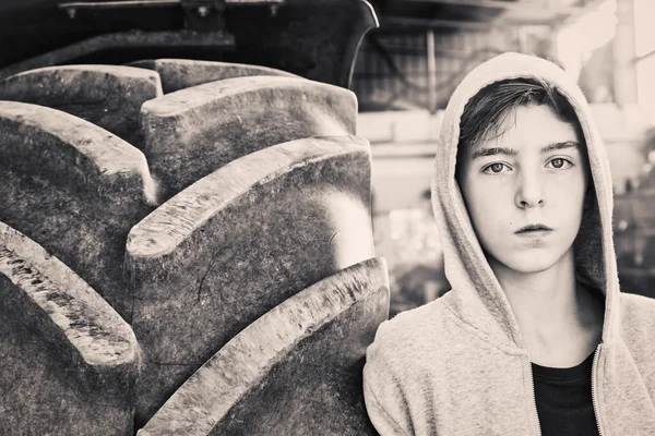 Portrait of a teenage boy leaning against a huge tire — Stock Photo, Image