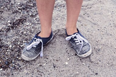 Sahilde eski kirli mavi ayakkabılar ile iki ayak