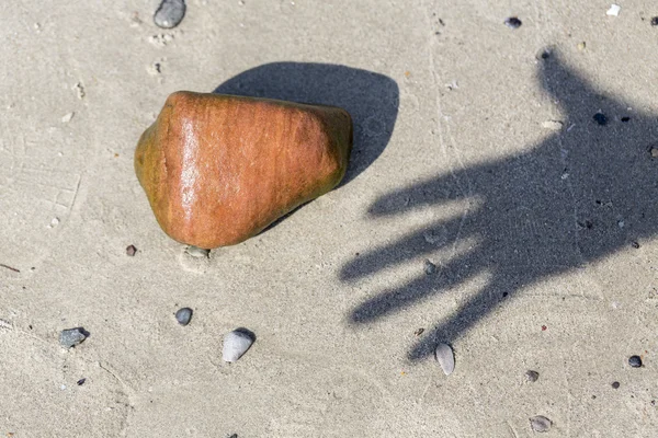 Schatten einer Hand und nasser Kieselstein am Strand — Stockfoto