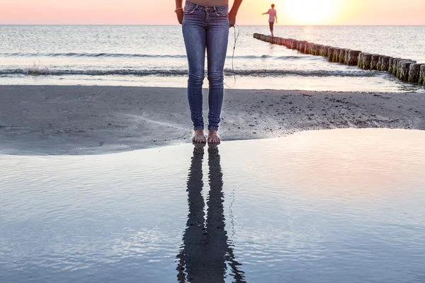 Die Beine einer Frau spiegeln sich im Ozean bei Sonnenuntergang — Stockfoto