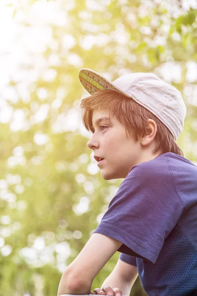 Perfil de un niño joven con la tapa de la base y hojas verdes borrosas en — Foto de Stock