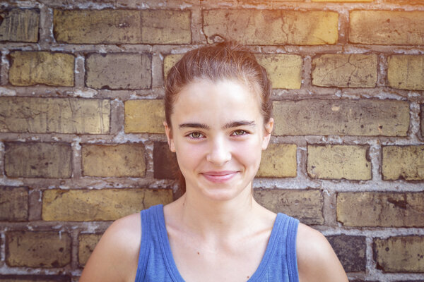 portrait of a smiling teenager girl leaning against a brick wall
