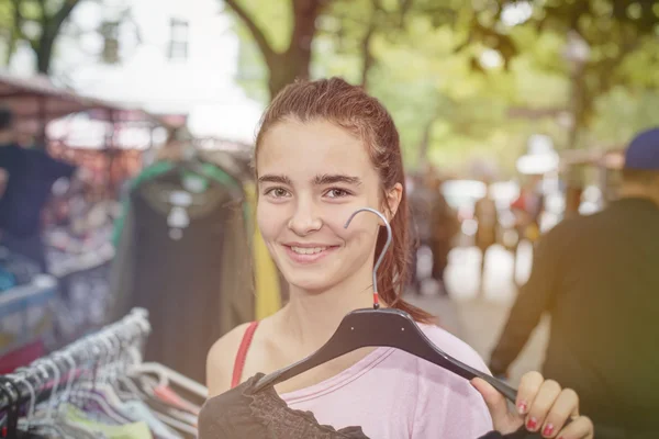 Mulher sorridente em um mercado de pulgas está segurando um cabide de roupas — Fotografia de Stock