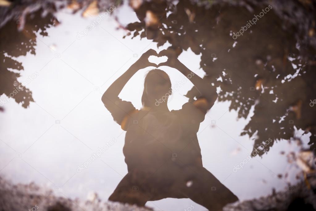 reflection in a puddle of a person who shapes a heart with his h