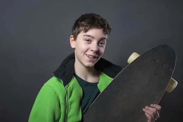 Fier adolescent souriant tenant sa longue planche, avec dos gris — Photo