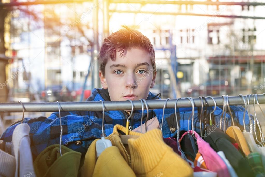 portrait of a teenage boy behind a clothes rail on a flea market