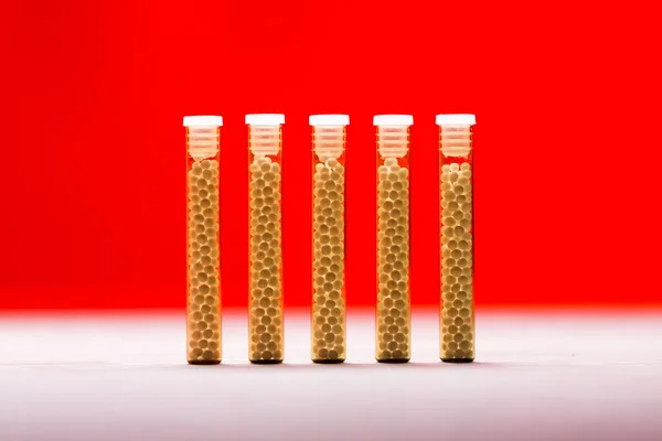 Five small glass tubes with homeopathy globules, red background — Stock Photo, Image