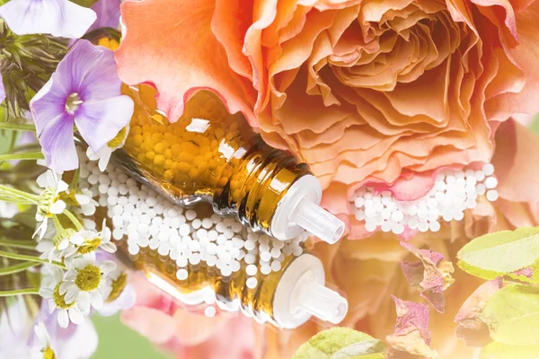 Botella con glóbulos homeopáticos colocados en un espejo con flores —  Fotos de Stock