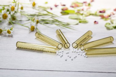 Homeopati küreleri ve çiçekleri olan küçük cam tüpler.