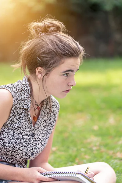 Tienermeisje is zittend op een weiland en schrijven — Stockfoto