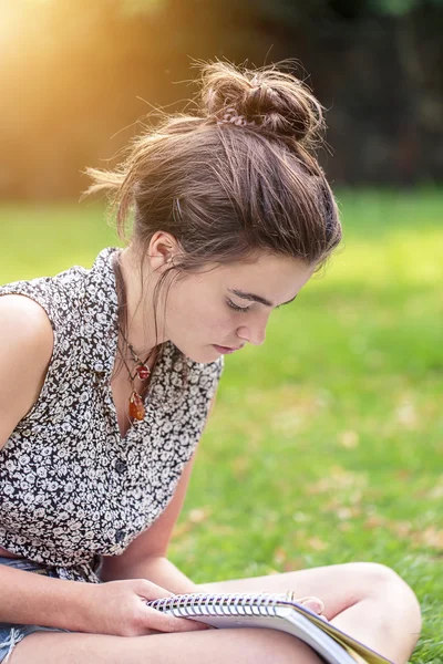 Teenager-Mädchen sitzt auf einer Wiese und schreibt — Stockfoto