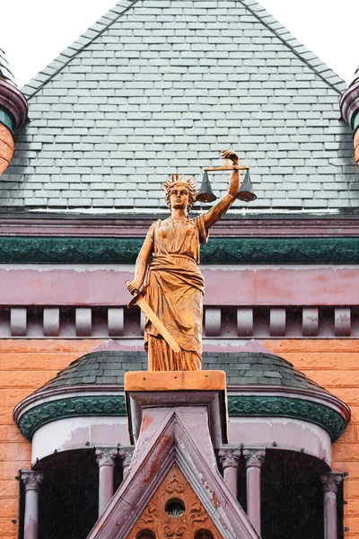 A bronze statue holding a sword and the scales of justice stands atop the roof of a historic Courthouse building in a small Monroe County Wisconsin Town.