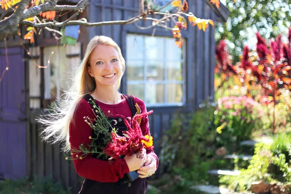 幸せな笑顔の女性の庭師は彼女のコテージの庭の外で花を持っていて — ストック写真