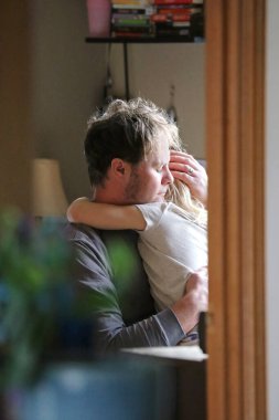 Sevgi dolu bir baba, ağlayan çocuğunu evinde kucaklıyor ve teselli ediyor..