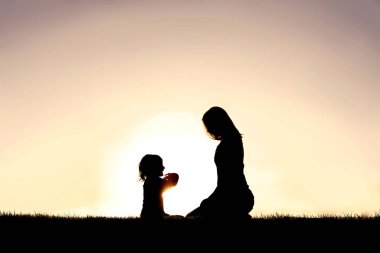 Gün batımında küçük çocuğuyla oturup konuşan genç bir Hristiyan annenin silüeti.