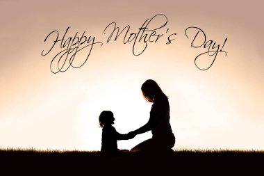 Bir Hıristiyan annenin silueti, dışarıda huzur içinde oturup dua etmek için küçük çocuğuyla konuşuyor ve el ele tutuşuyor. Gökyüzünde günbatımına karşı, 