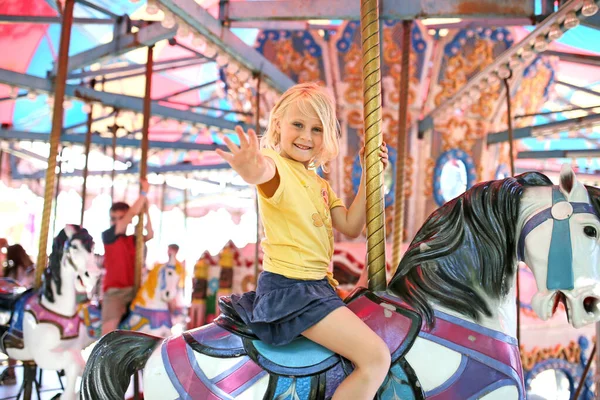 在小镇的狂欢节上 一个快乐的小女孩骑着马兜风 向摄像机招手 — 图库照片