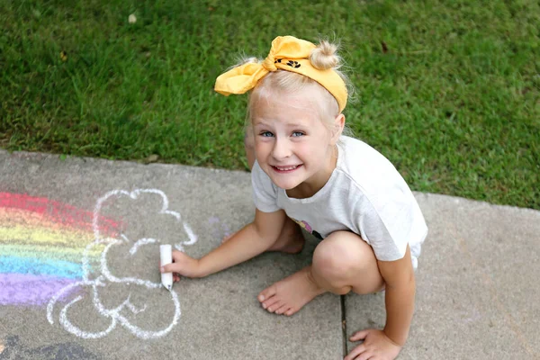 귀여운 소녀가 여름날 분필로 밖에서 무지개에 색칠을 있습니다 — 스톡 사진