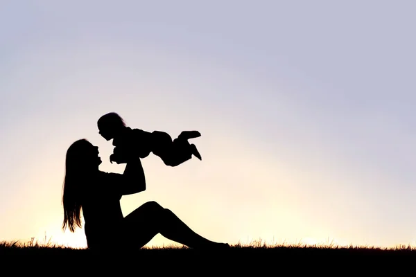 Silhouette einer glücklichen Mutter, die draußen mit einem lachenden Baby spielt — Stockfoto