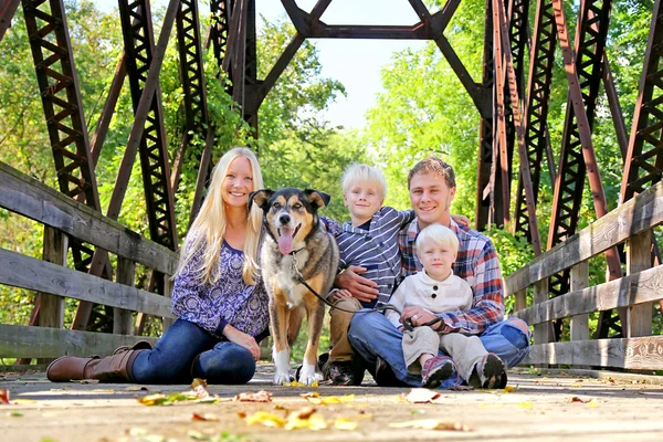 Familie van vier mensen en hond zittend op brug in het najaar van — Stockfoto