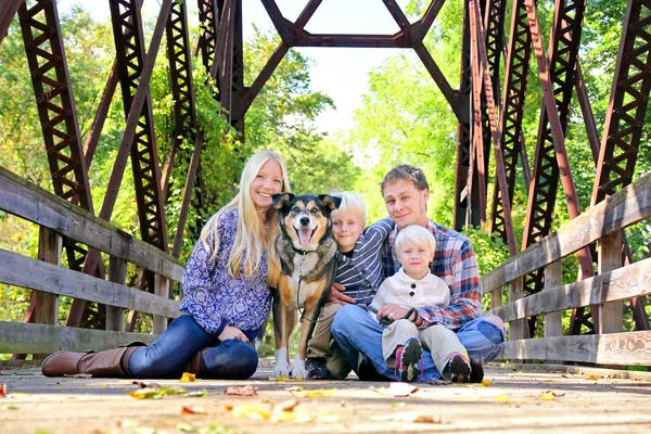 Vierköpfige Familie mit Hund sitzt im Herbst auf Brücke — Stockfoto