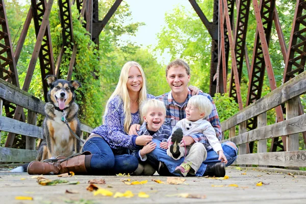 Riendo, familia feliz sentada en el puente en el bosque de otoño — Foto de Stock