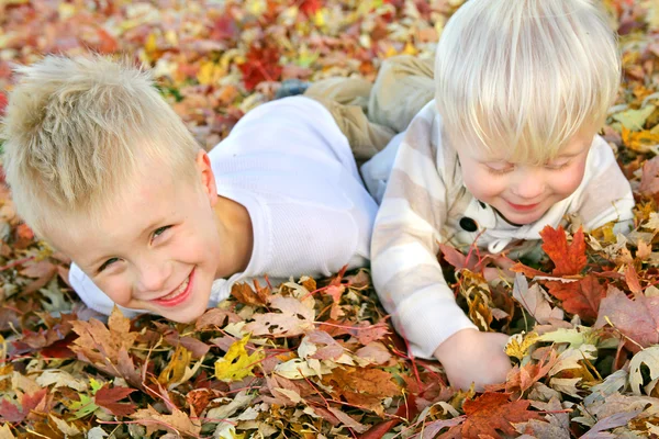 Två unga barn leker i höst löv högen — Stockfoto